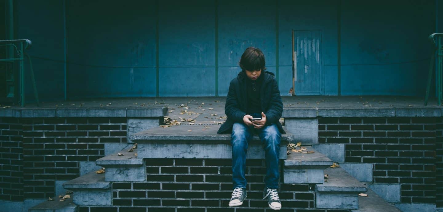 Junge sitzt alleine mit Smartphone auf Treppe