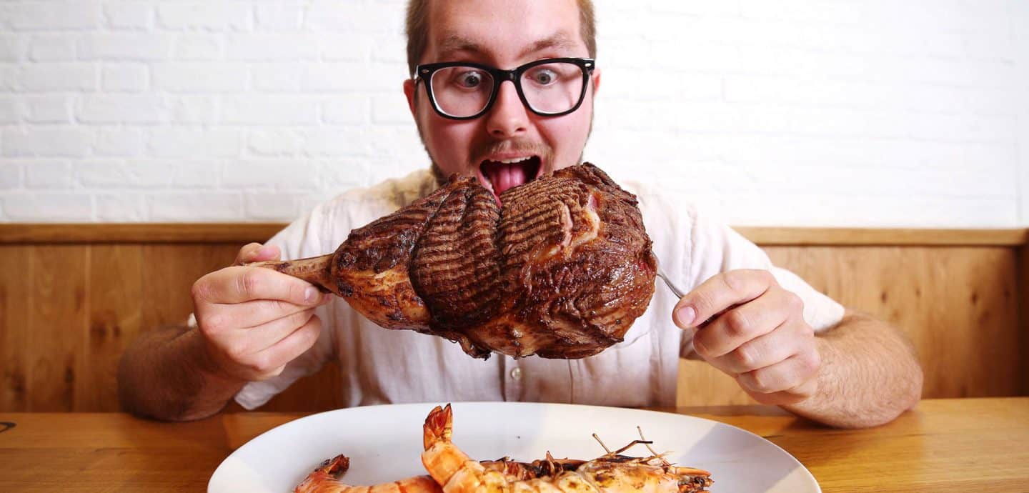 Ein Mann verspeißt ein großes Stück Fleisch. Foto: picture alliance/ Joe Pepler/ PinPep/ Cover Images