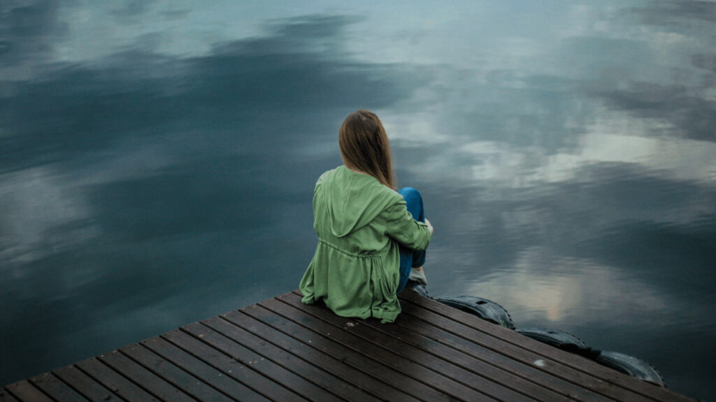 Eine Frau sitzt alleine auf einem Steg und guckt auf das Wasser.