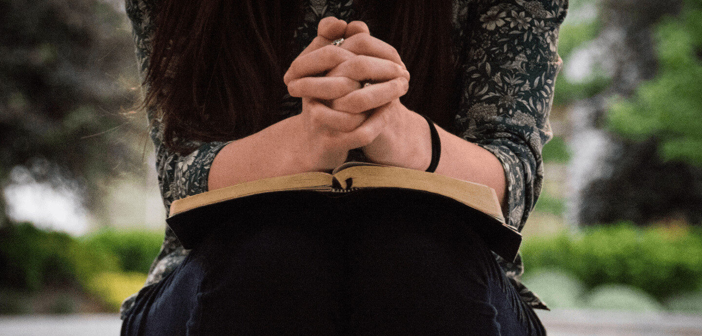 Frau betet mit gefalteten Händen auf einem Buch