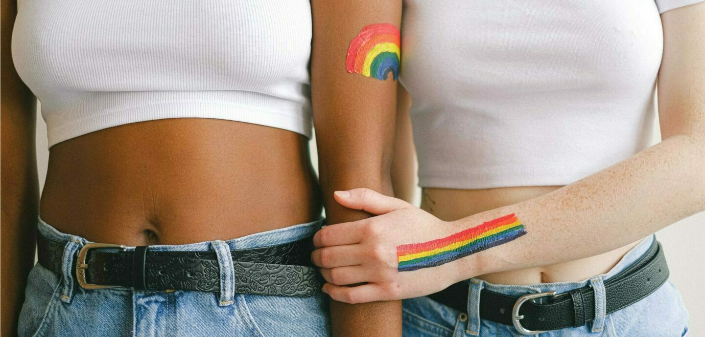 Zwei Mädchen halten Händchen und haben regenbogen auf die Arme gemalt