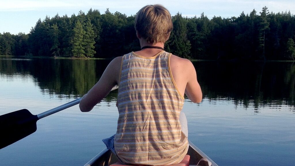 Ein Junge, von hinten abgebildet, rudert über einen See