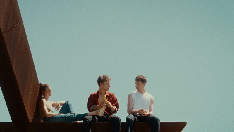 Drei junge Menschen sitzen auf einer Mauer in der Sonne.