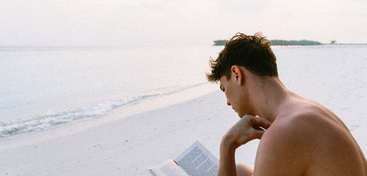 Person liegt am Strand und liest Reiselektüren
