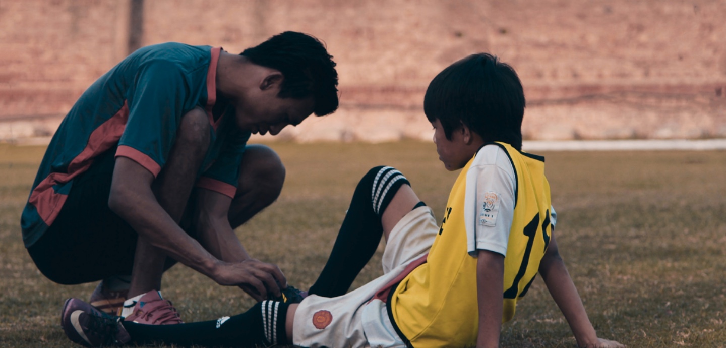 Kind sitzt verletzt auf dem Boden, Trainer untersucht das Knie