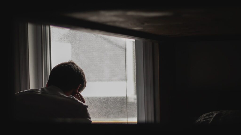 Ein Junge der verzweifelt aus dem Fenster schaut.