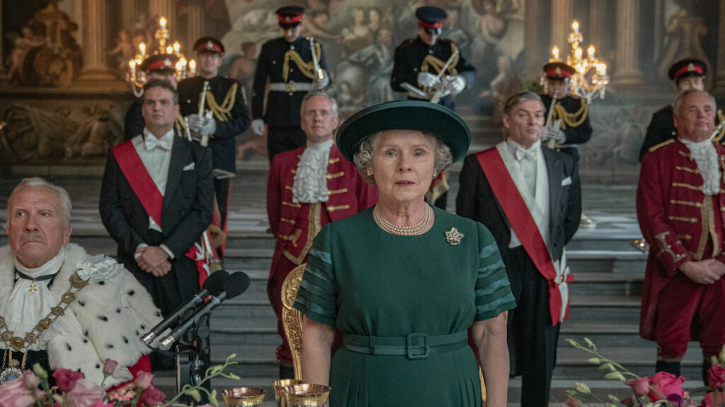 Queen Elizabeth II. stehend und eine Rede haltend. Hinter ihr verschiedene Würdenträger.