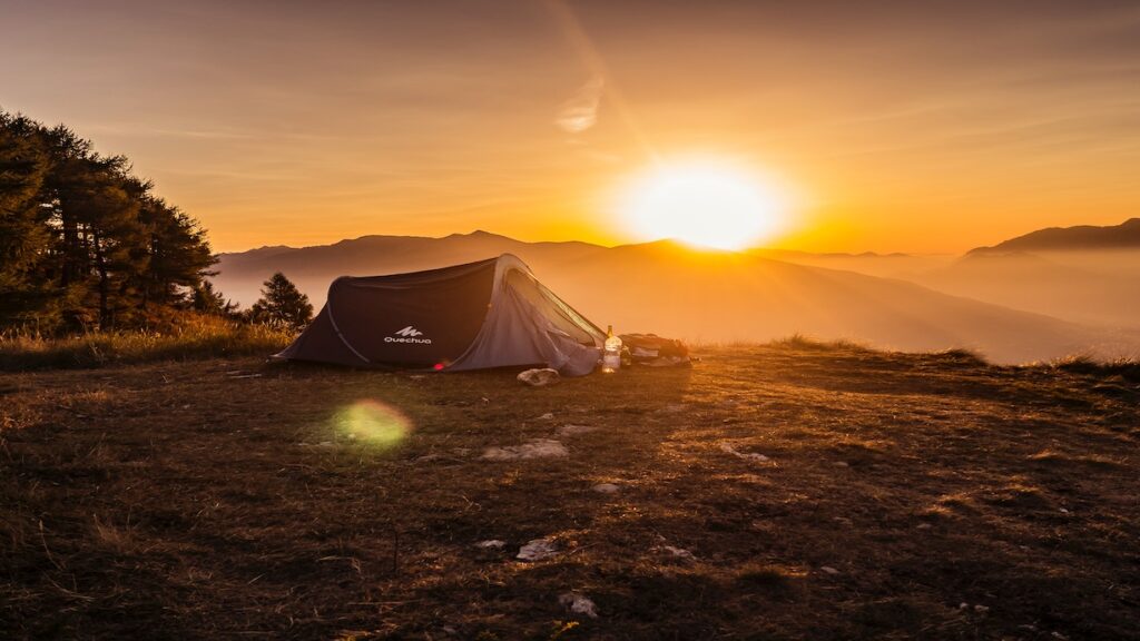 Camping-Zelt auf einer Wiese mit Sonnenaufgang im Hintergrund.