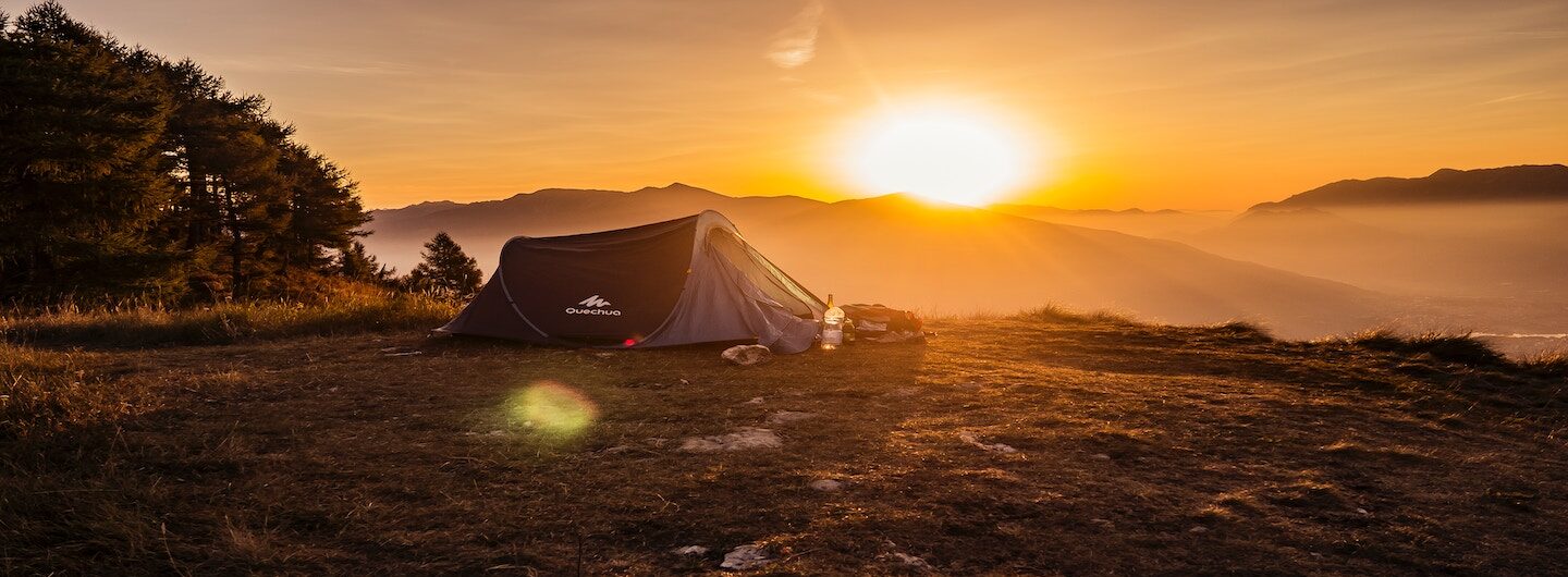 Camping-Zelt auf einer Wiese mit Sonnenaufgang im Hintergrund.