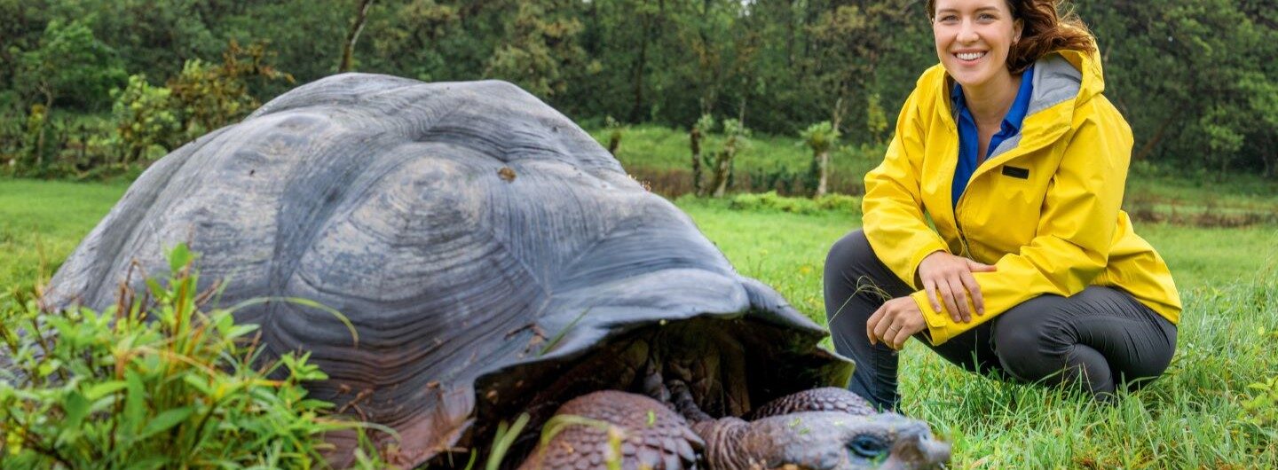 Hannah Emde, Wildtierärztin kniet in kurzer Distanz hinter einer, in freier Wildbahn lebenden Riesenschildkröte.